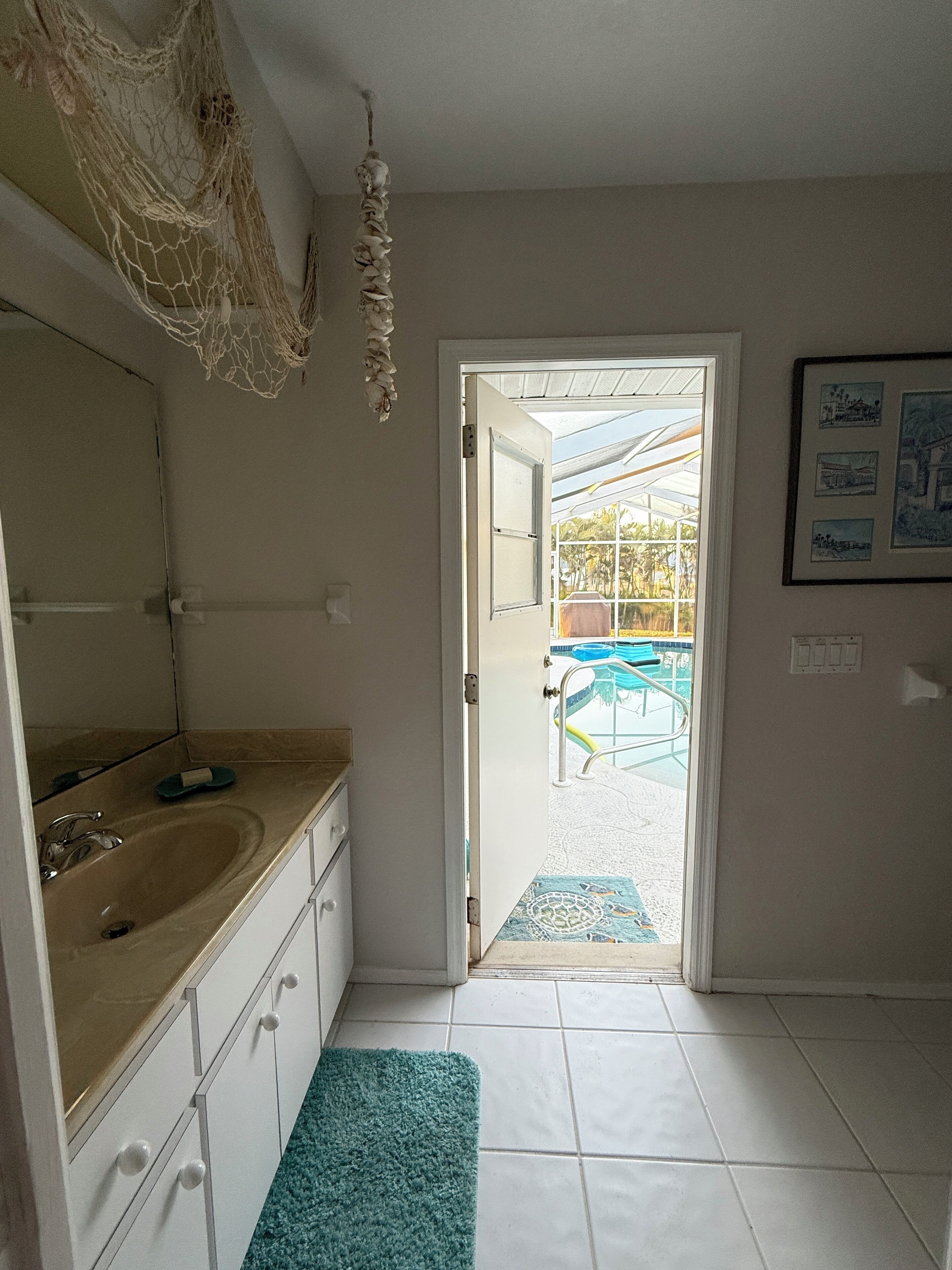 Une salle de bain avec un lavabo, un miroir et une vue sur l’espace extérieur de la piscine, accessible par une porte ouverte.