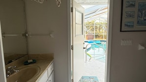 A bathroom with a sink, mirror, and a view of an outdoor pool area through an open door.
