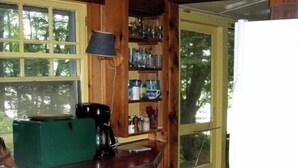 A compact kitchen with wooden cabinets, a coffee maker, and a refrigerator. - Shelving Rock Camp on Squam Lake (Center Harbor)