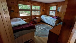 A cabin bedroom with two beds, a wooden floor, a round rug, and large windows. - Shelving Rock Camp on Squam Lake (Center Harbor)