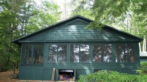 A green wooden cabin with large windows, a covered entrance, and a yellow kayak in front. - Shelving Rock Camp on Squam Lake (Center Harbor)