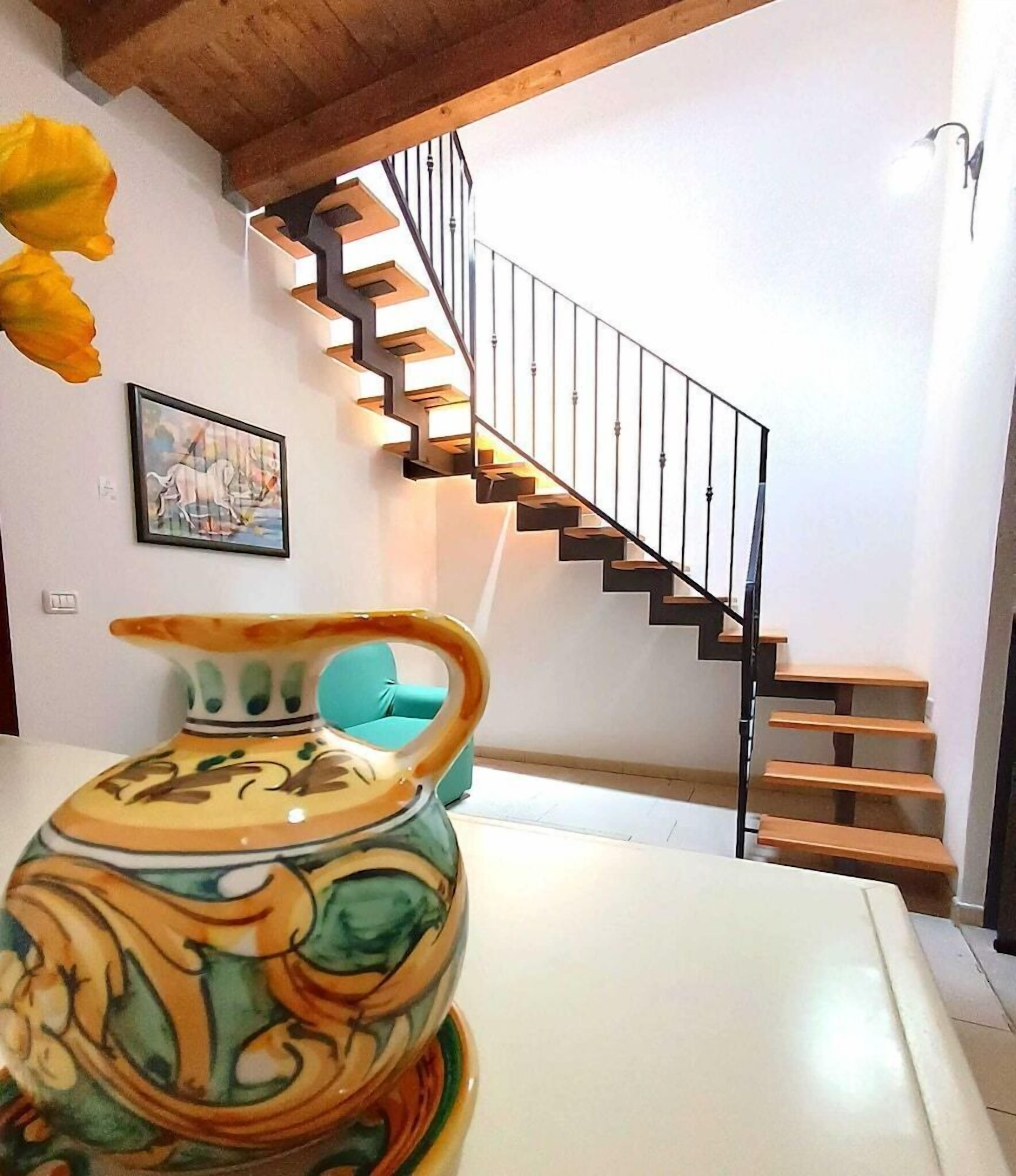 Un interno moderno con una scala, un vaso decorativo e un quadro appeso al muro.