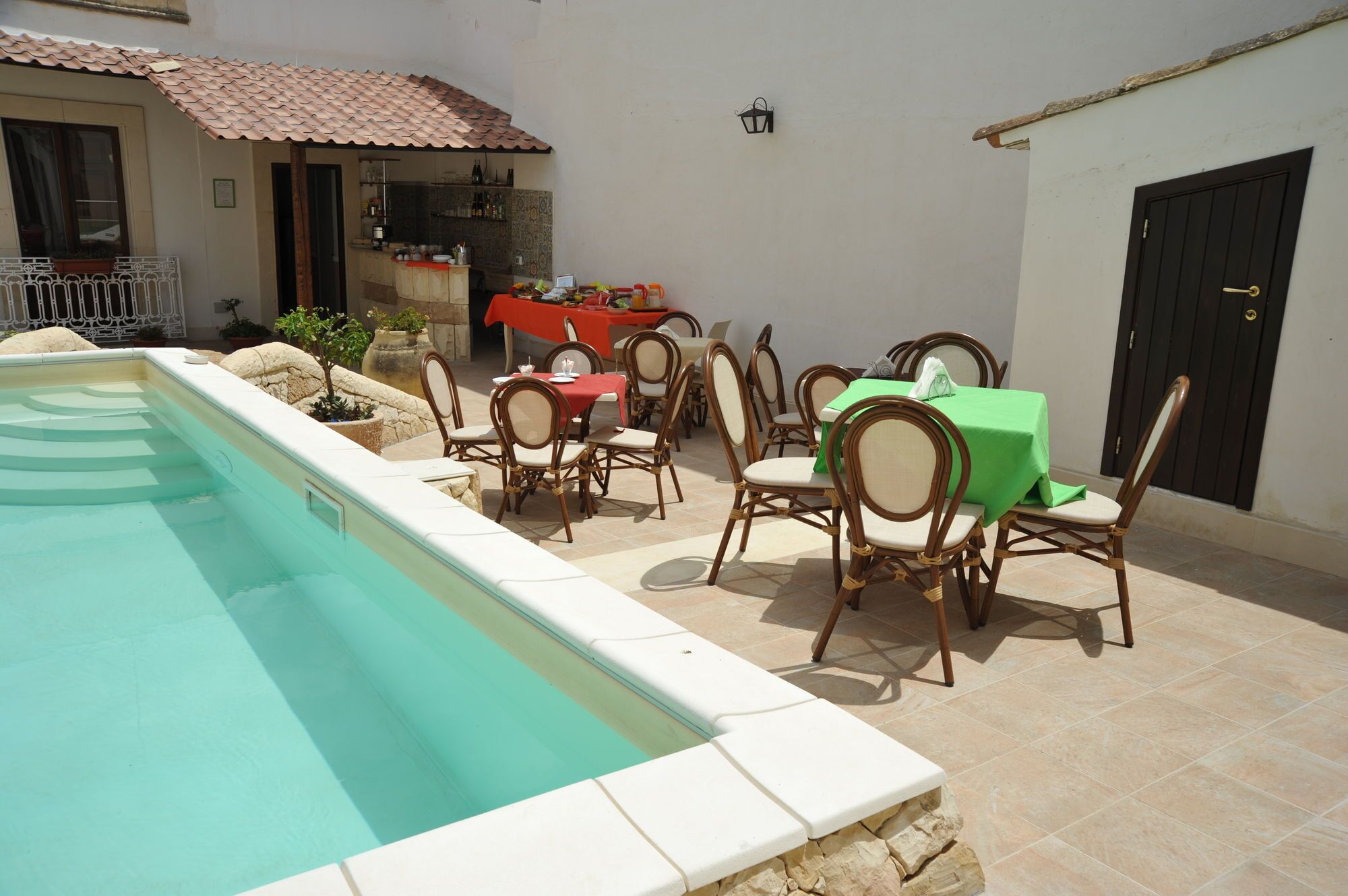Area piscina con zona pranzo completa di sedie e tavoli, angolo cottura e una porta.