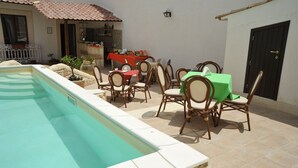 Un espace aménagé au bord de la piscine, comprenant un coin repas avec des chaises et des tables, un espace cuisine et une porte.