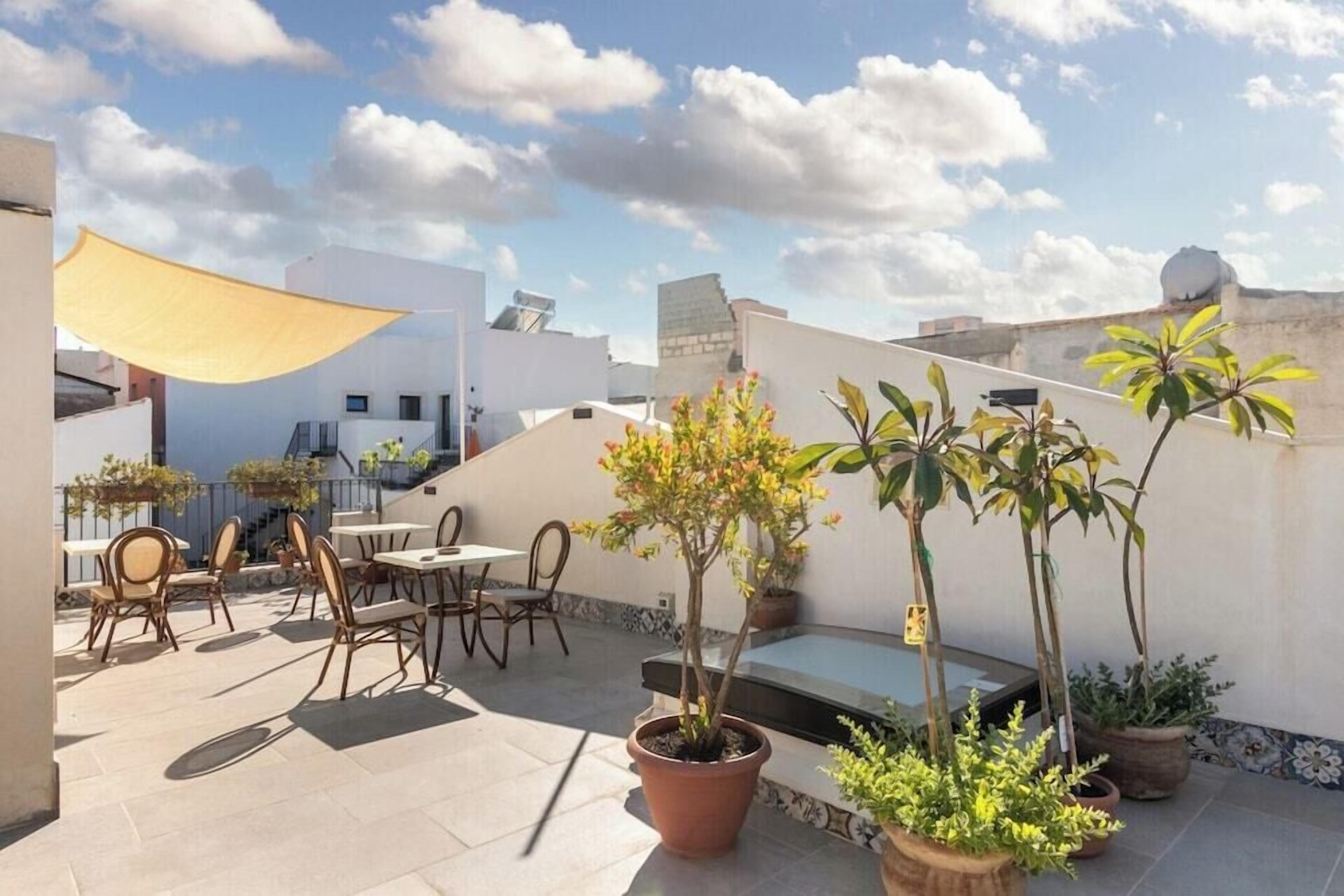 Una terrazza sul tetto con posti a sedere all'aperto, piante in vaso e un tenda vela gialla.