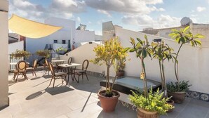 Une terrasse sur le toit avec des espaces de détente en plein air, des plantes en pot et un auvent jaune.