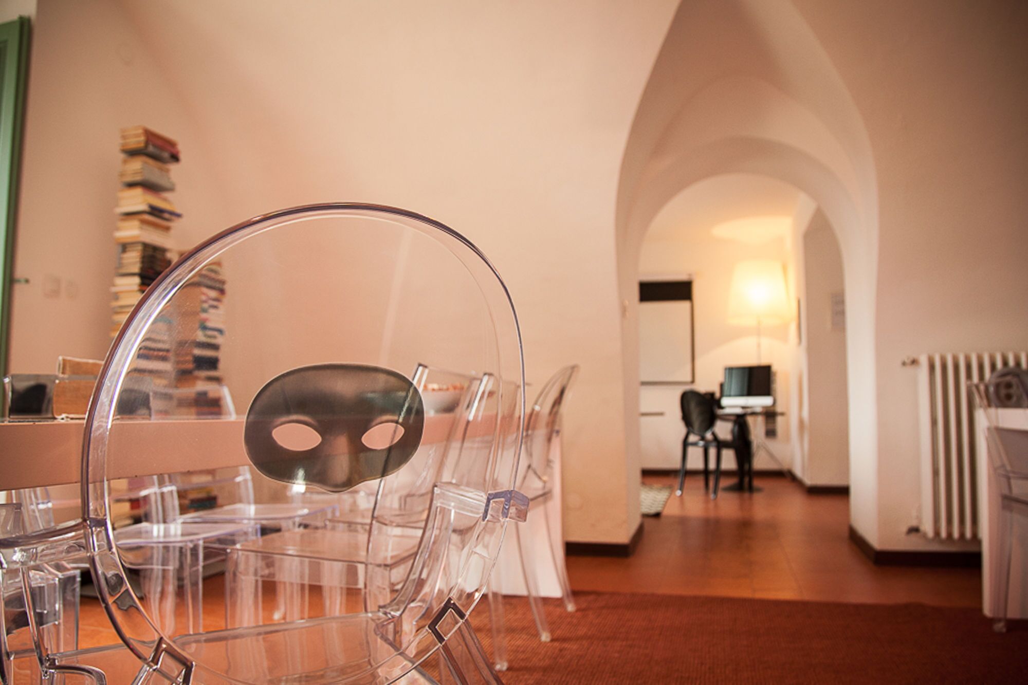Un'area pranzo moderna con sedie in plastica trasparente e un tavolo, un corridoio ad arco che conduce a una zona cucina con un computer e delle sedie.