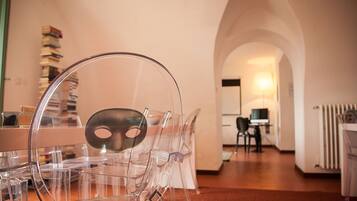 Un'area pranzo moderna con sedie in plastica trasparente e un tavolo, un corridoio ad arco che conduce a una zona cucina con un computer e delle sedie.