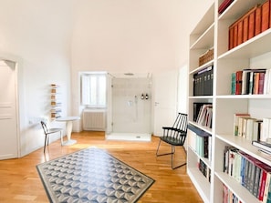 Et værelse med bogreol, radiator, brusebad og et tæppe med et mønster.
