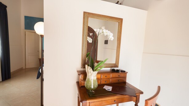 A wooden dresser with a mirror, a vase with white orchids, and a pair of glasses on the dresser. - Villa Giuliana (Licata)