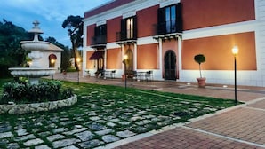 A building with a red and white facade, a fountain, outdoor seating, and a well-maintained garden. - Villa Giuliana (Licata)
