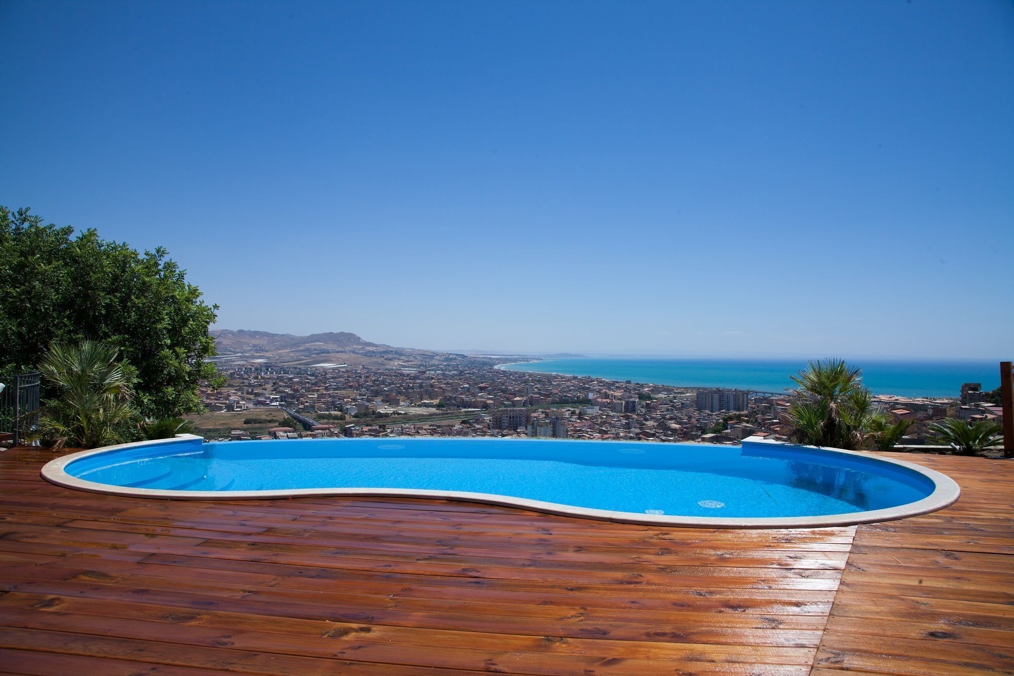 A wooden deck with a swimming pool overlooking a coastal cityscape.