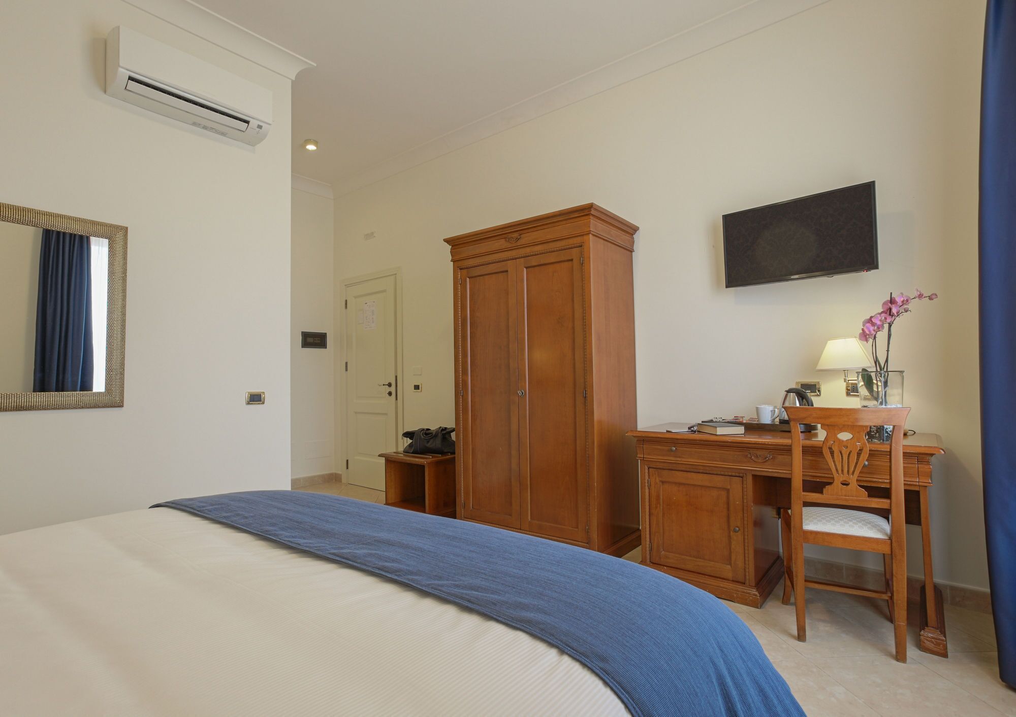 A hotel room with a bed, a wardrobe, a desk with a chair, a television, and a window with curtains.
