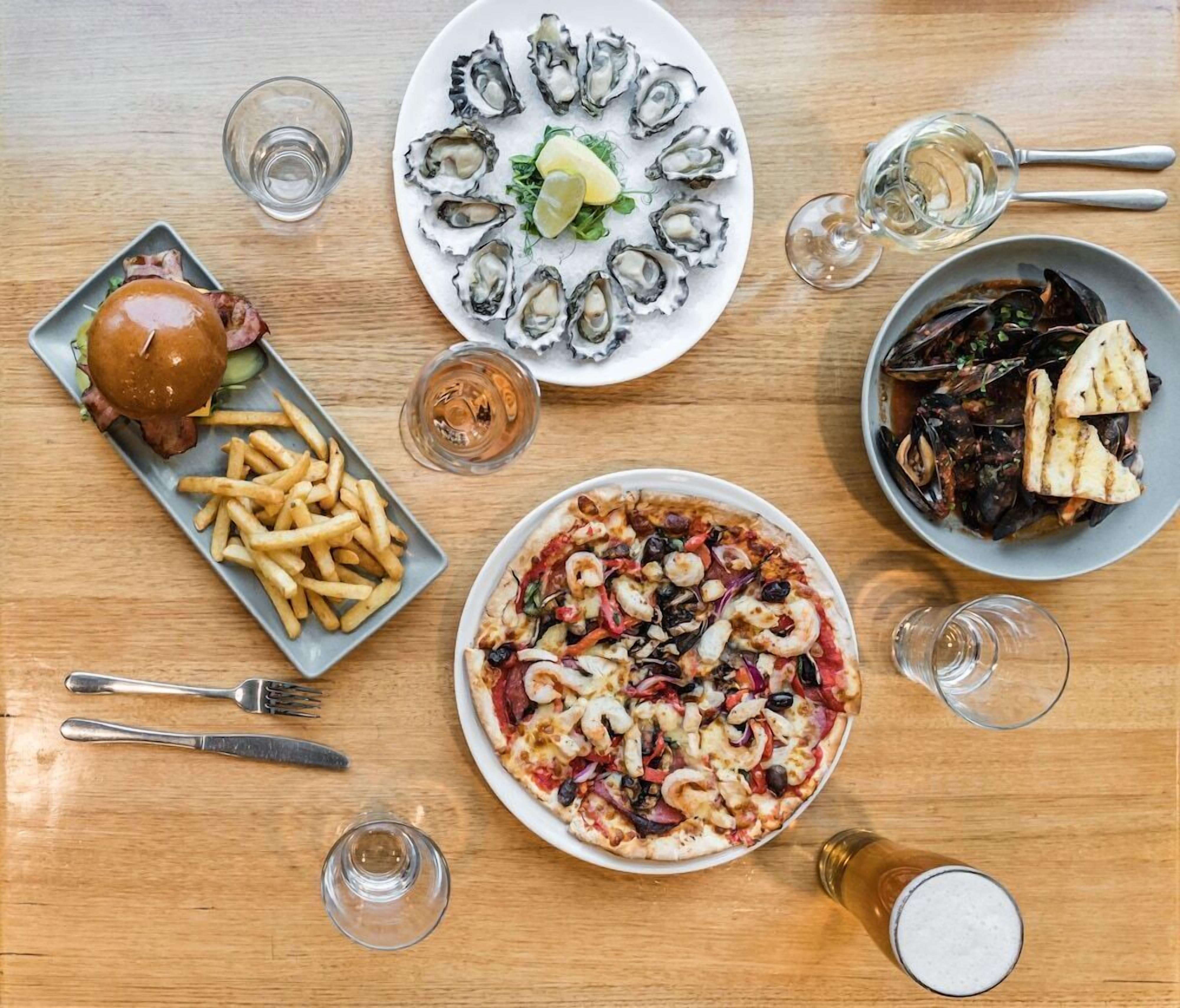 A dining table with various dishes including seafood, a burger, and fries, along with cutlery and glasses.