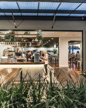 Een modern café met een houten toonbank, plantenrekken en een zithoek met tafels en stoelen.