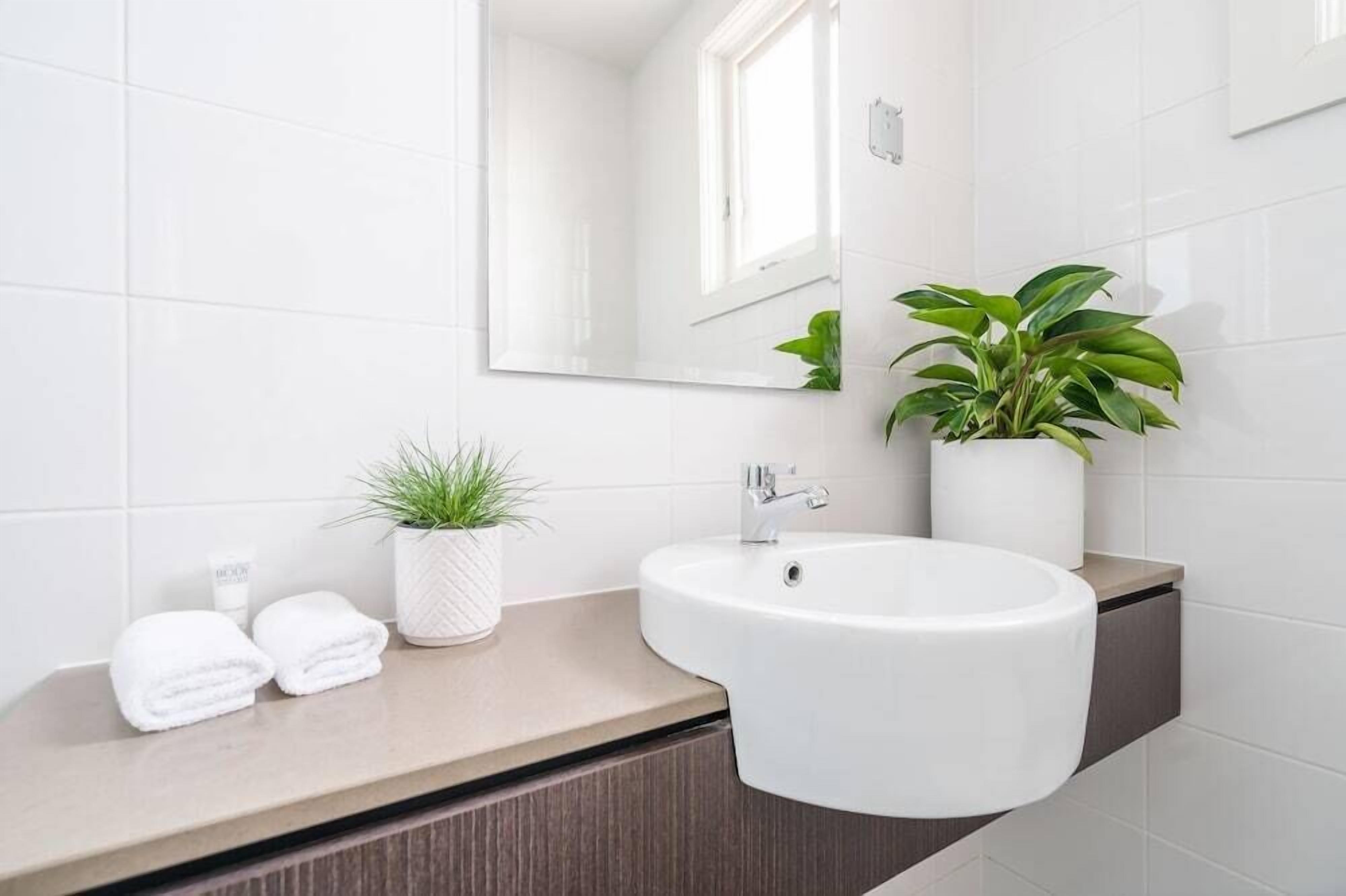 Un baño moderno con un lavamanos blanco, un espejo, una planta en maceta y toallas dobladas con cuidado sobre el mostrador.