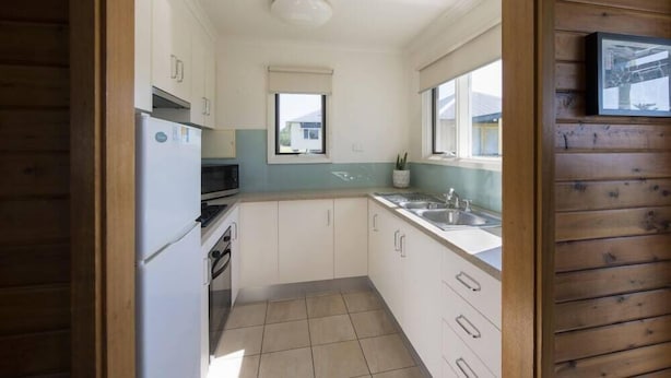 A compact kitchen with white cabinets, a built-in oven, a microwave, and a window above the sink. - West Beach Parks Resort (Adelaide)