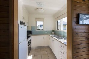 A compact kitchen with white cabinets, a built-in oven, a microwave, and a window above the sink.