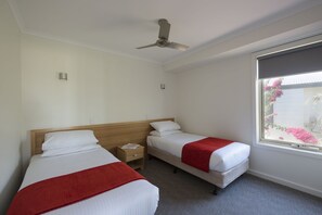 A hotel room with two beds, a ceiling fan, a window with a view of flowers, and a small bedside table with a lamp. - West Beach Parks Resort (Adelaide)