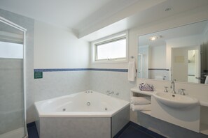 A modern bathroom with a bathtub, a sink, and a large mirror. - West Beach Parks Resort (Adelaide)