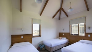 A room with two beds, wooden beams, a window, and a bag on the floor. - West Beach Parks Resort (Adelaide)