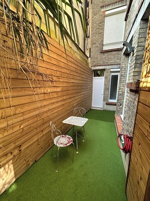 A small patio with two metal tables and chairs, a wooden fence, and a brick wall. - La Cour Barbatre | Terrasse (Reims)