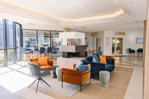 A modern hotel lobby with a seating area, a fireplace, and a view of the city through large windows. - Thalazur Ouistreham (Ouistreham)