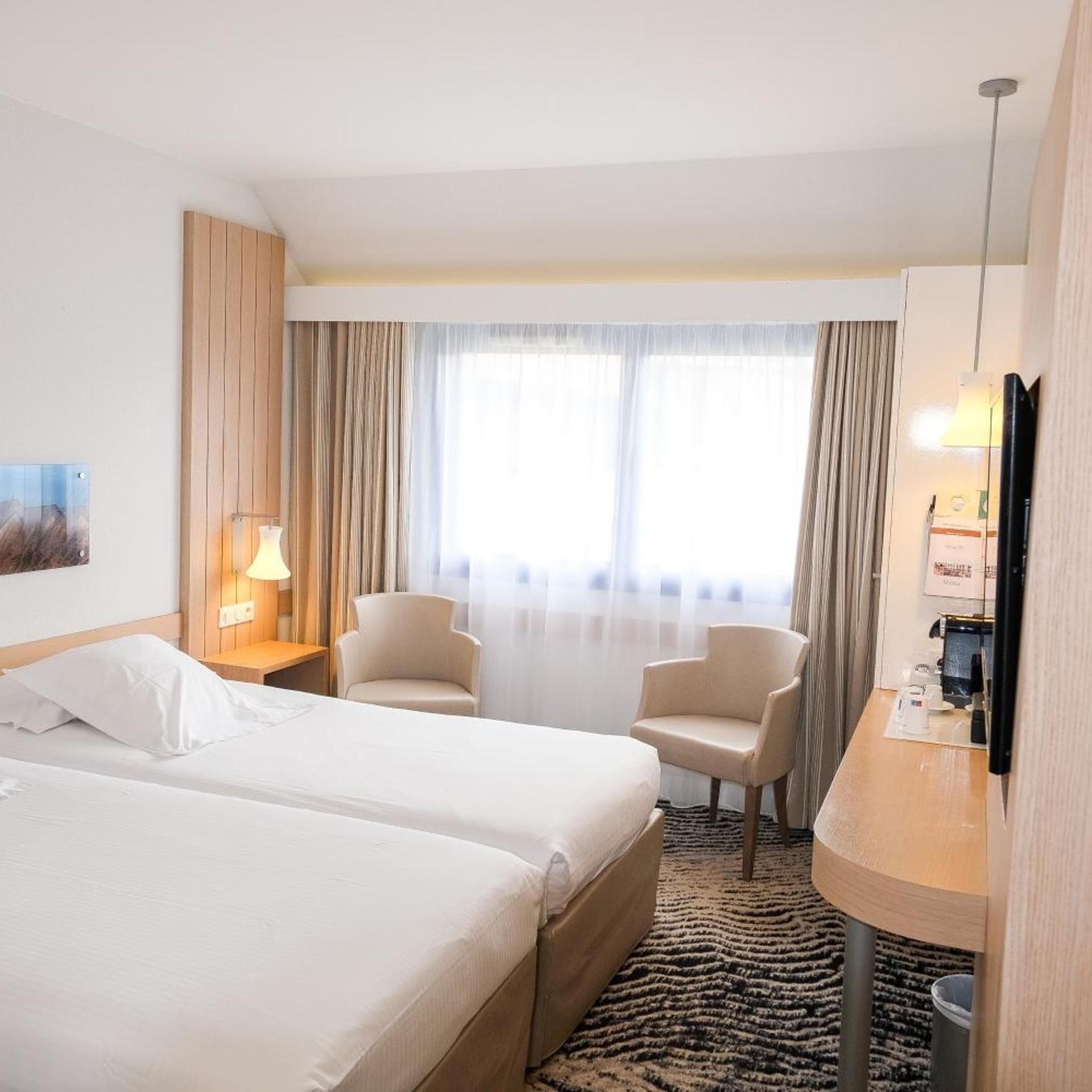 A hotel room with two beds, a desk, a chair, a TV, and a window with curtains.