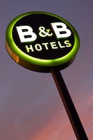 Un letrero circular con el texto "B&B HOTELS" sobre un cielo al anochecer.