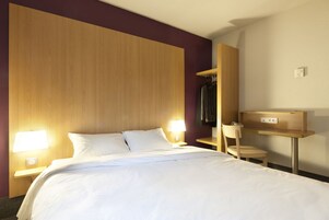 Habitación de hotel con una cama grande, dos lámparas de noche, una mesita, una silla y un espejo.