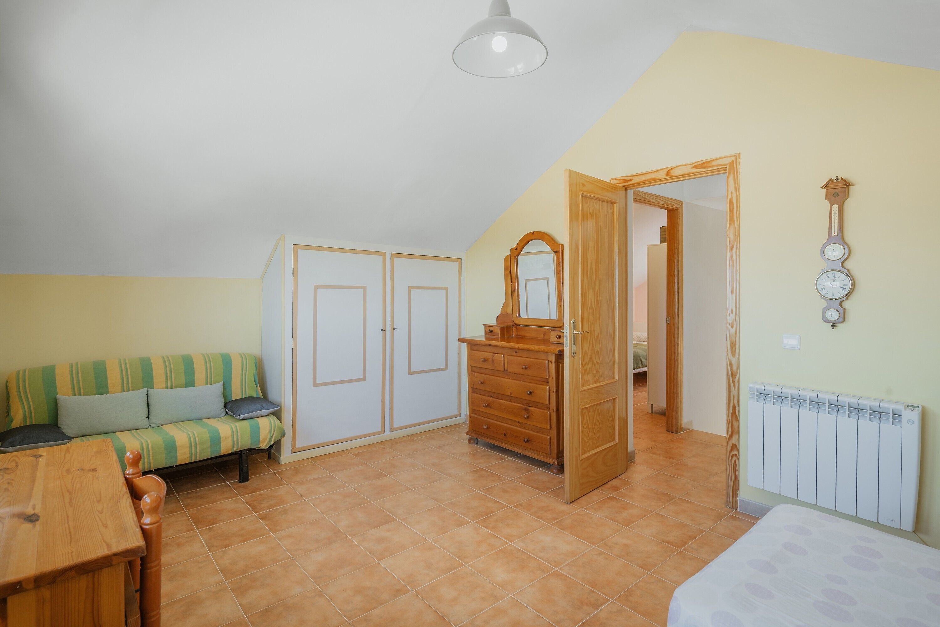 Una habitación con sofá, cómoda de madera, espejo, radiador y una puerta que da a otra estancia.