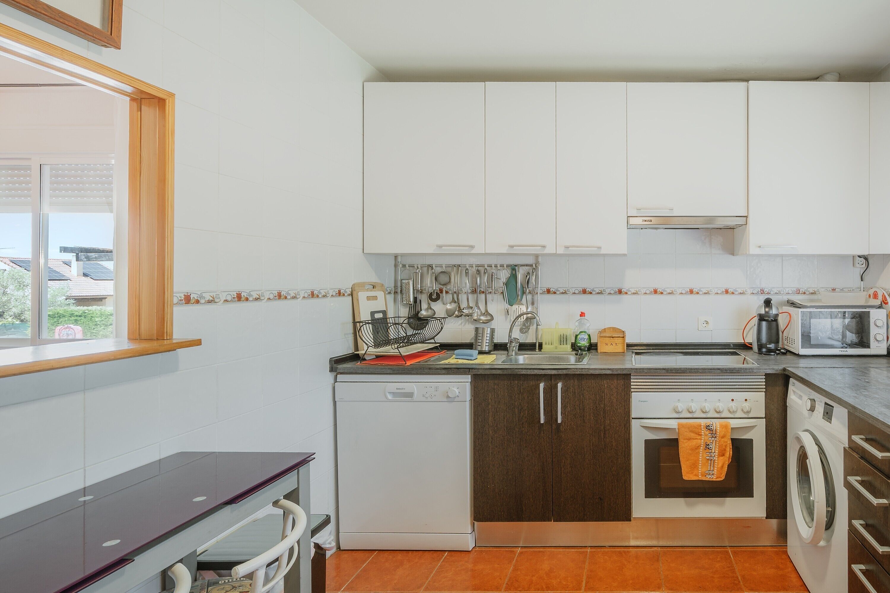 A compact kitchen with white cabinets, a dishwasher, an oven, a microwave, and a washing machine.