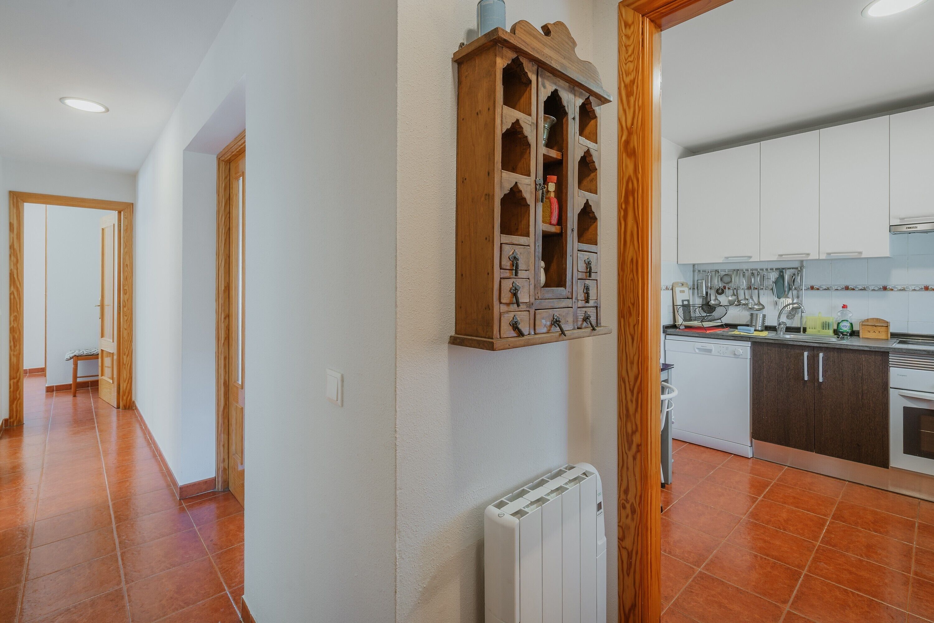 A kitchen with white cabinets, a wooden cabinet with multiple drawers, a white radiator, and a tiled floor.