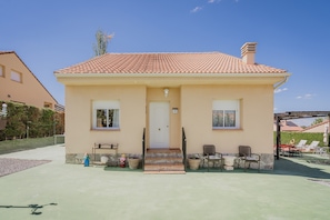 A two-story house with a tiled roof, a front door, and a small porch with chairs.
