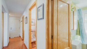 A hallway with a wooden door, a white cabinet, and a bed with floral bedding. - Casa Rural El Robledal with Private Pool near Segovia & Madrid, Sleeps 8 (Zarzuela del Monte)