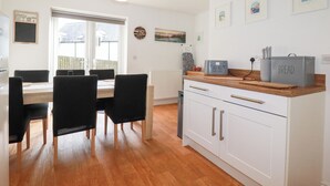 A modern kitchen with white cabinets, a wooden countertop, and a dining area with a table and chairs. - Poldam (St Austell)