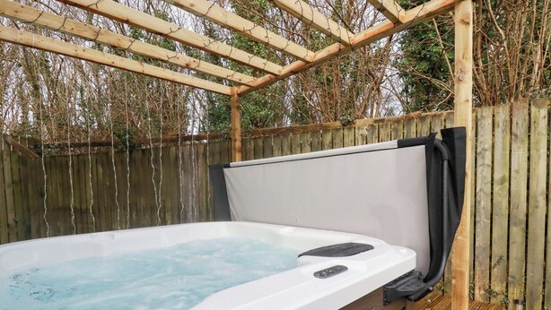 A hot tub with a wooden pergola overhead, surrounded by a wooden fence and trees. - Poldam (St Austell)