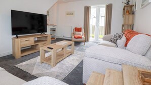 A modern living room with a flat-screen TV, wooden furniture, a sofa, and a sliding glass door leading to a balcony. - Poldam (St Austell)