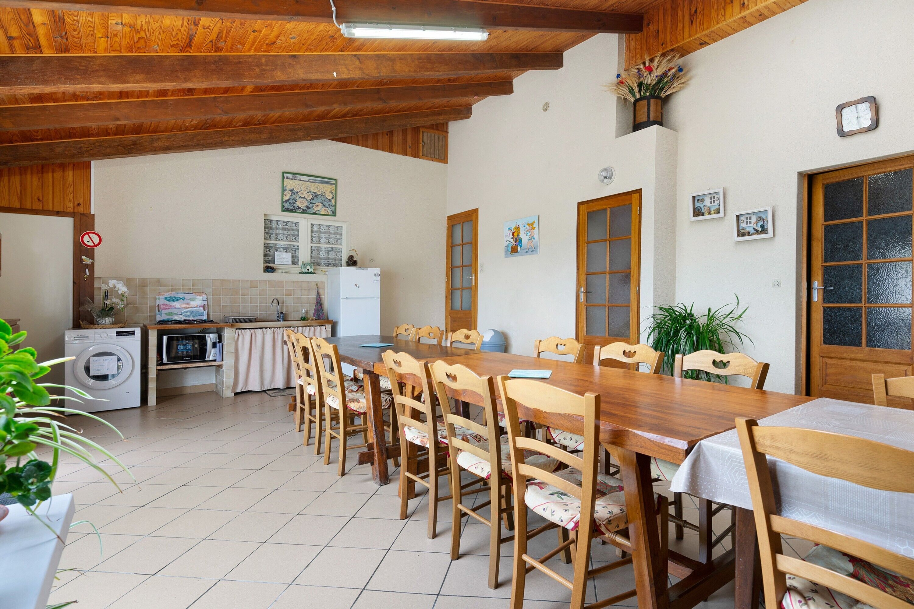 A dining area with wooden chairs and a table, a kitchen with appliances, and a ceiling with exposed beams.