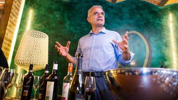 Uma pessoa em pé num bar, com garrafas e copos de vinho.