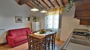 A compact kitchen with a dining area, a red sofa, wooden chairs, and a tiled floor. - Pelagaccio (Peccioli)
