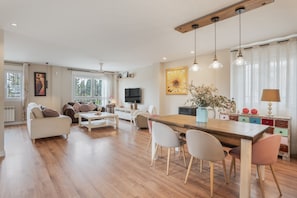 A spacious living room with a wooden dining table, a sofa, and a TV.