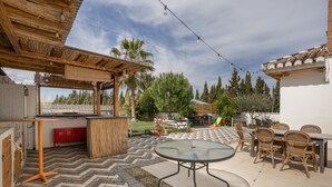 Een terras buiten met een tafel en stoelen, een houten pergola en een speelruimte op de achtergrond.