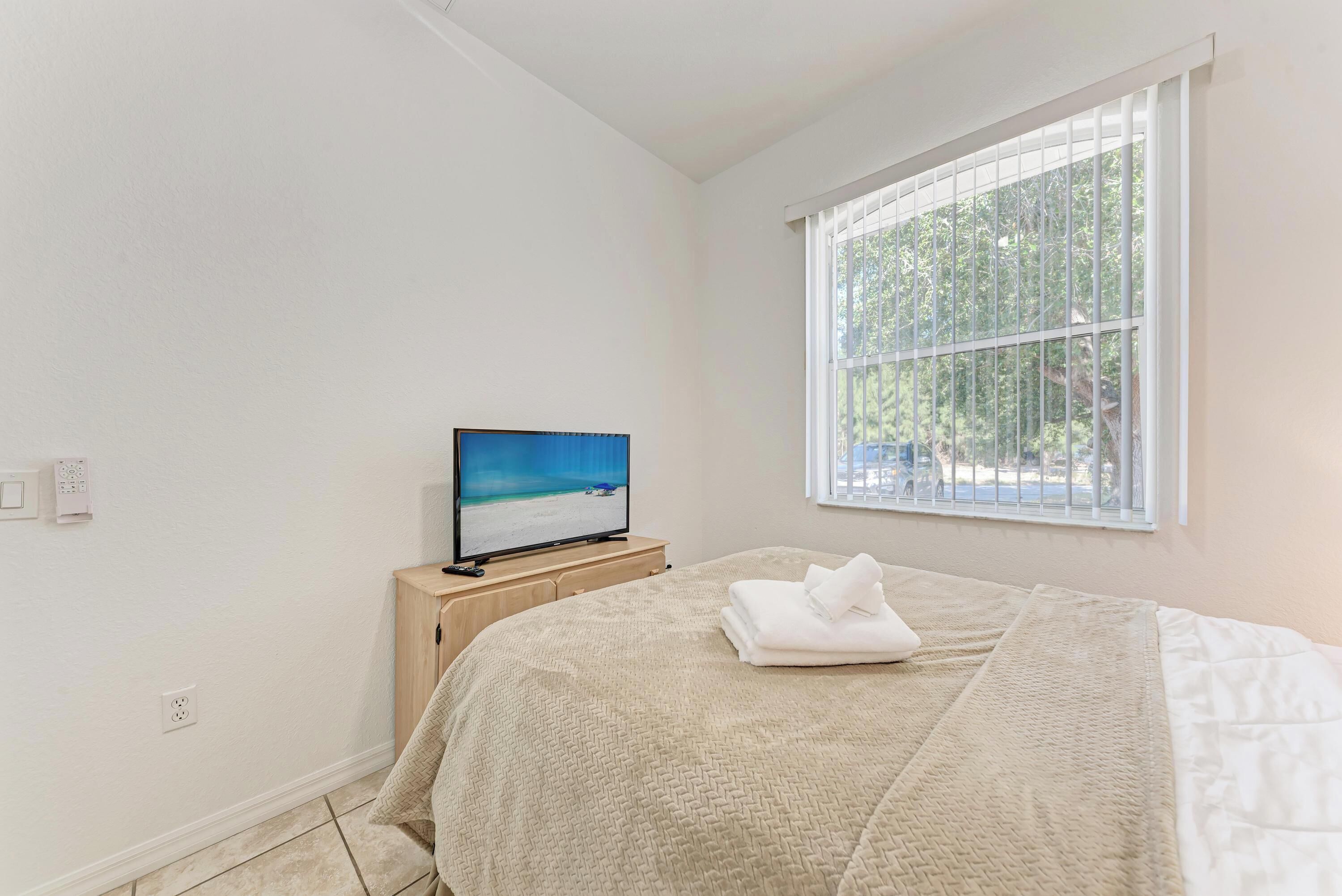 Una camera da letto con un letto, una TV su un mobile in legno, una finestra con persiane e vista su del verde all'esterno.