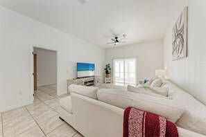 Een ruime woonkamer met een grote bank, een televisie en een plafondventilator.