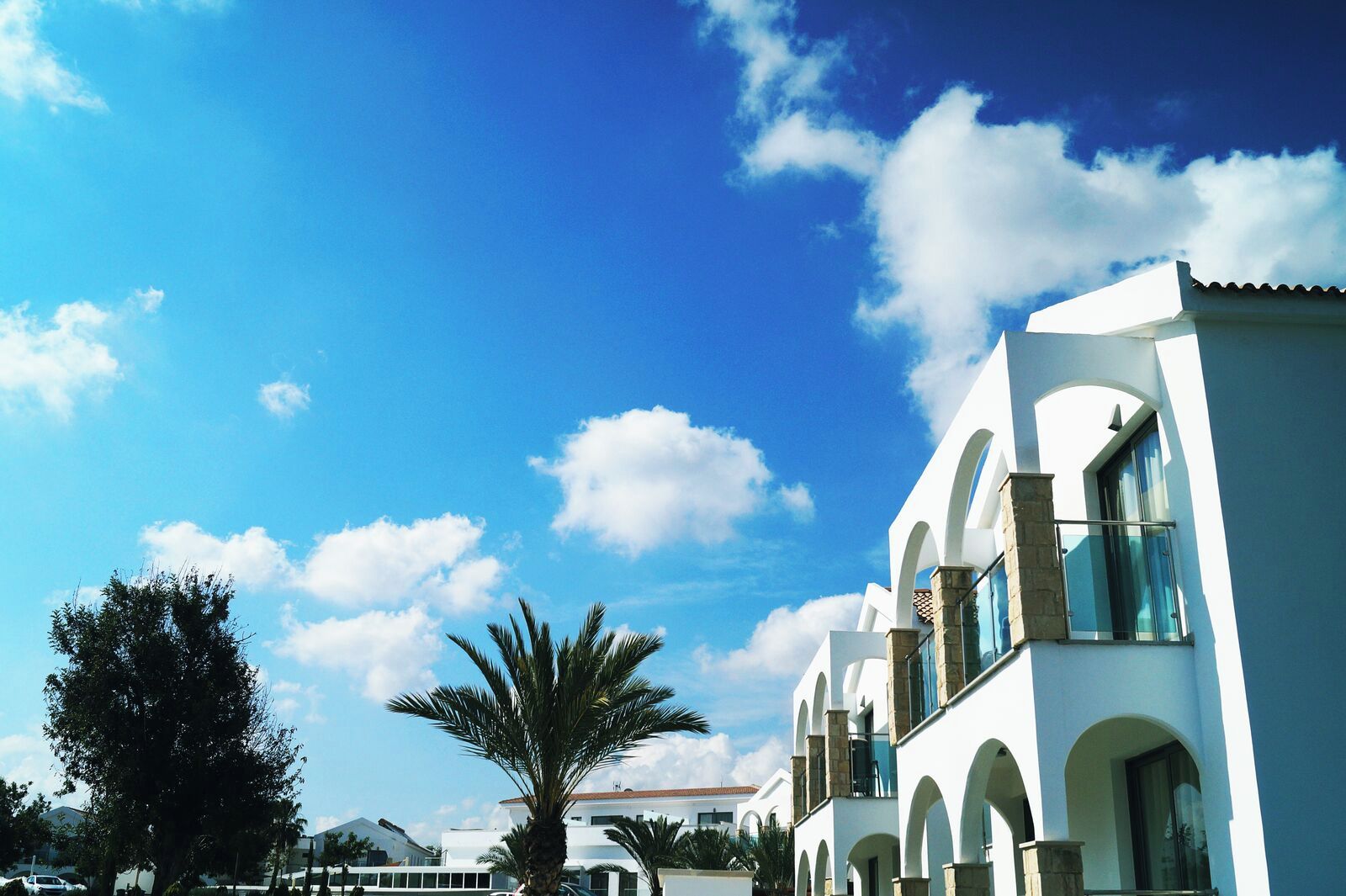 A white building with arched windows and balconies, a clear blue sky, and palm trees.