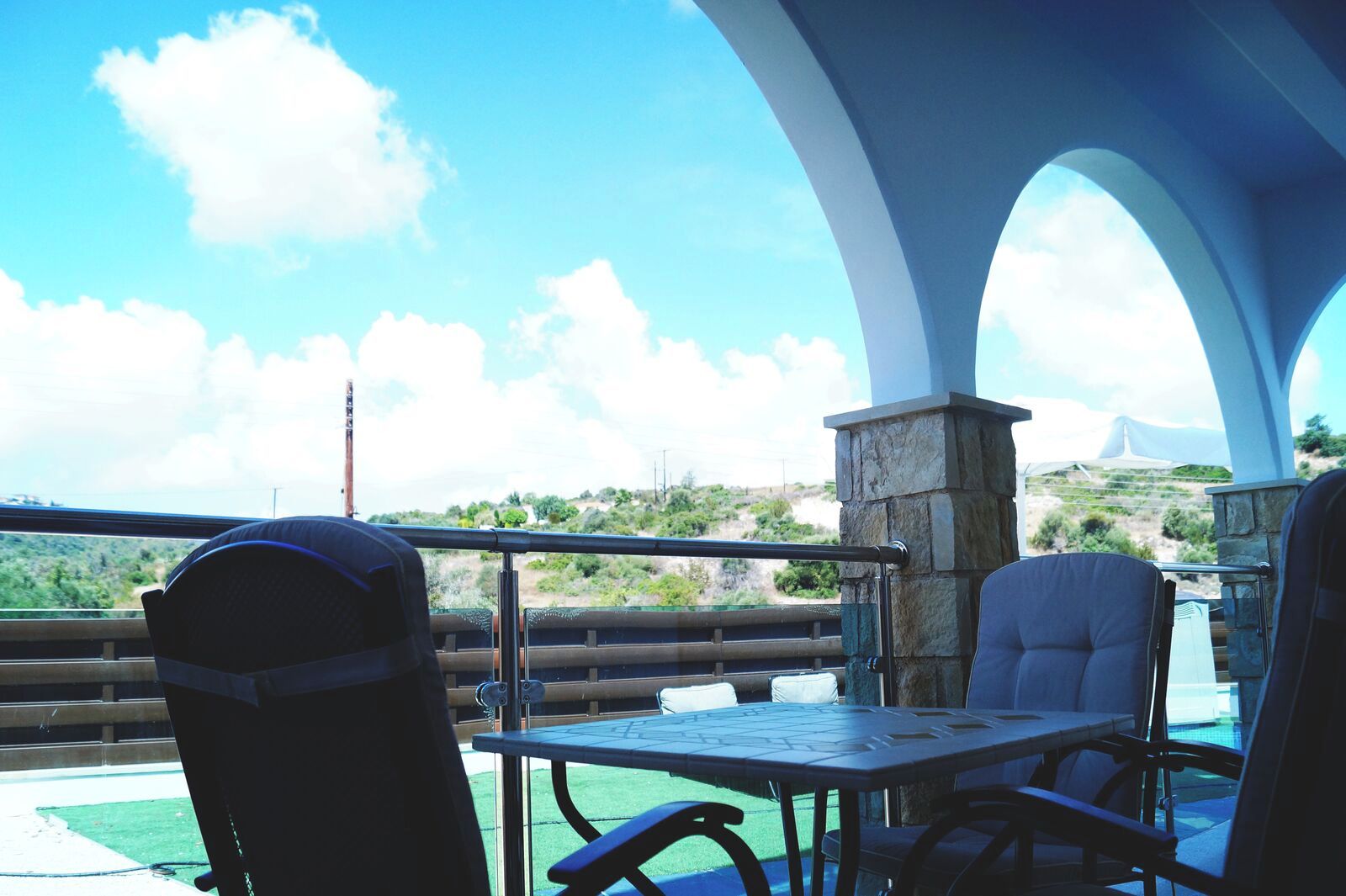 An outdoor seating area with a table and chairs, a stone pillar, and a view of the landscape.