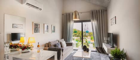 Un salon moderne comprenant un canapé, un téléviseur et un coin repas, avec une grande fenêtre offrant une vue sur la verdure.