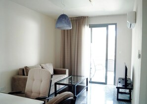A modern living room with a sofa, armchair, glass coffee table, and a television on a stand. - Latchi Escape Hotel and Suites (Neo Chorio)