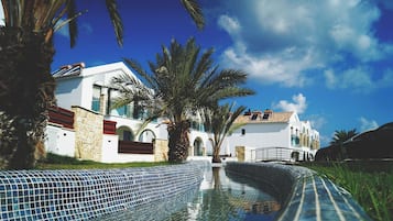 A modern building with a pool, palm trees, and a clear blue sky.
